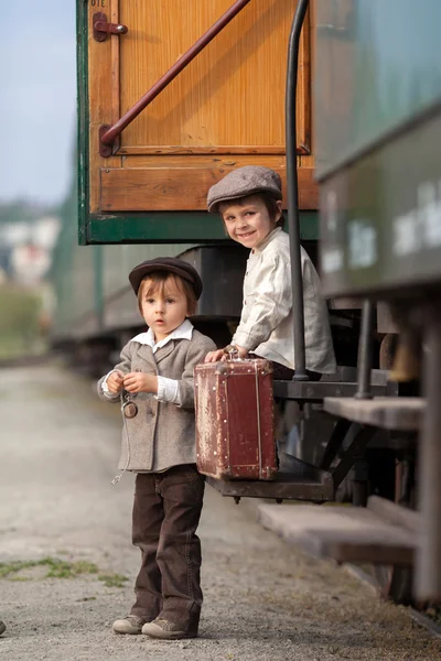 Dois meninos, vestidos com roupas vintage e chapéu, com mala — Fotografia de Stock