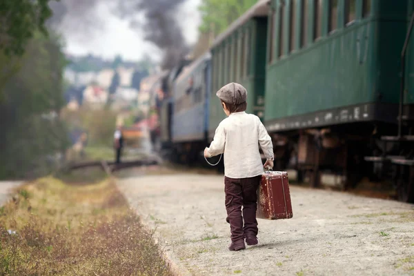 Poika, pukeutunut vintage-paitaan ja hattuun, matkalaukun kanssa — kuvapankkivalokuva