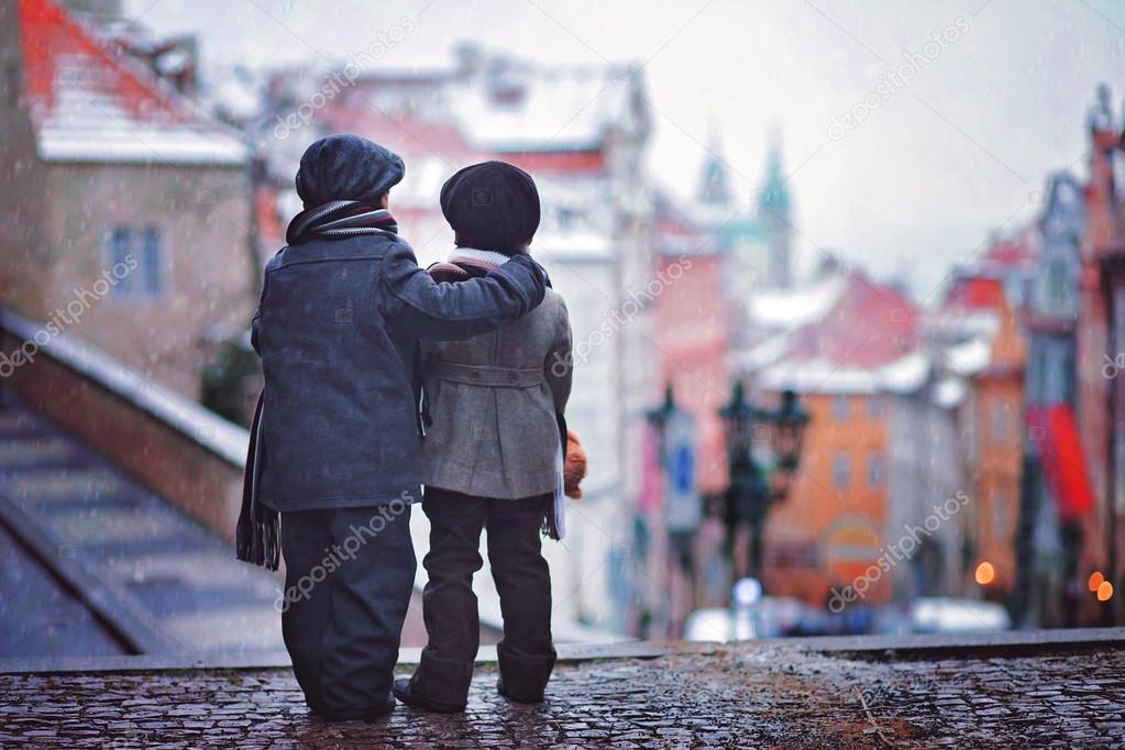 Two kids, standing on a stairs, view of Prague behind them, snow