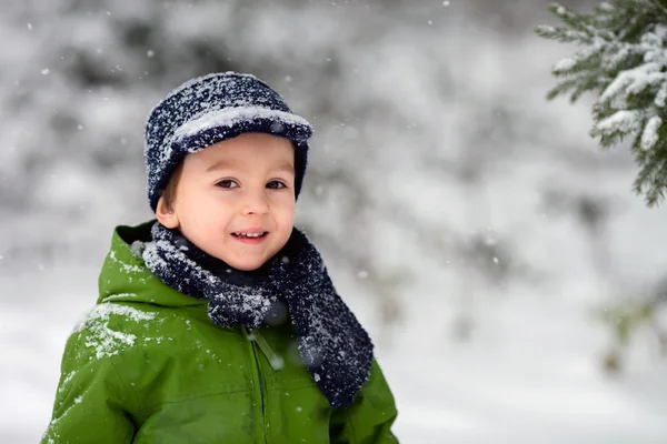 Entzückender kleiner Junge, der an einem verschneiten Tag draußen Schneeflocken bläst — Stockfoto