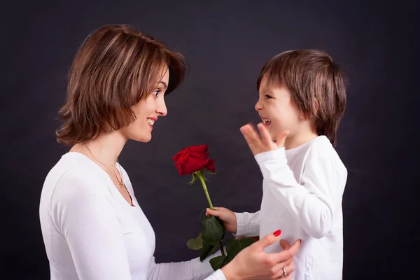 Jovem garoto dando lindo rosa vermelha para sua mãe — Fotografia de Stock