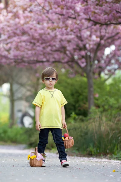 Kleiner süßer Junge, der zwei Körbe mit Blumen und Eiern trägt, geht — Stockfoto