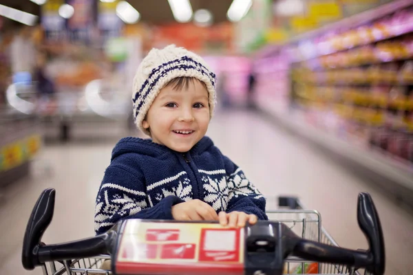 Menino adorável, sentado em um carrinho de compras — Fotografia de Stock