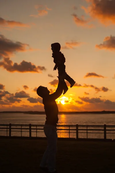 Padre arrojando a su hijo en el aire en la playa, silueta s — Foto de Stock