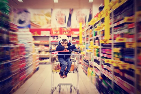 Entzückender kleiner Junge, der in einem Einkaufswagen sitzt — Stockfoto