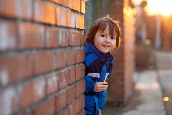 Adorable little boy, next to brick wall, eating chocolate bar on — Stock Photo, Image