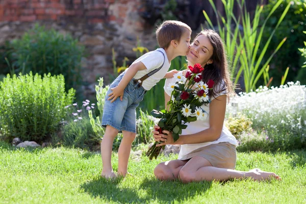 Beautiful kid and mom in spring park, flower and present. Mother — Stock Photo, Image