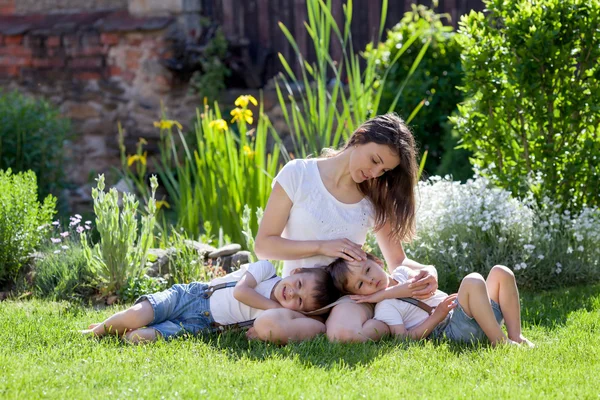 Jovem mãe e seus dois filhos, meninos, sentado em um gramado, tendem — Fotografia de Stock