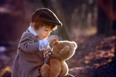 Adorable little boy with his teddy bear friend in the park clipart