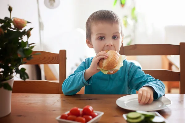 Beautiful little boy, eating sandwich at home, vegetables on the — Stock Photo, Image