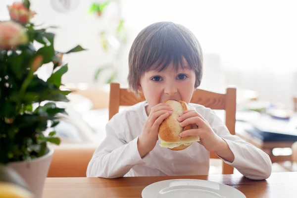 Vacker liten pojke, äta smörgås hemma, grönsaker på den — Stockfoto