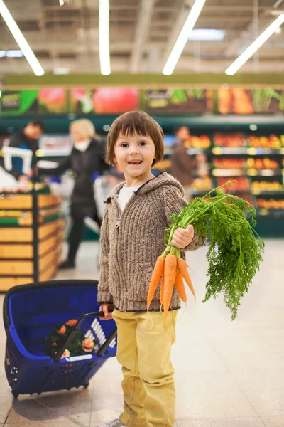 Bonito menino pequeno e orgulhoso ajudando com compras de supermercado, saudável — Fotografia de Stock