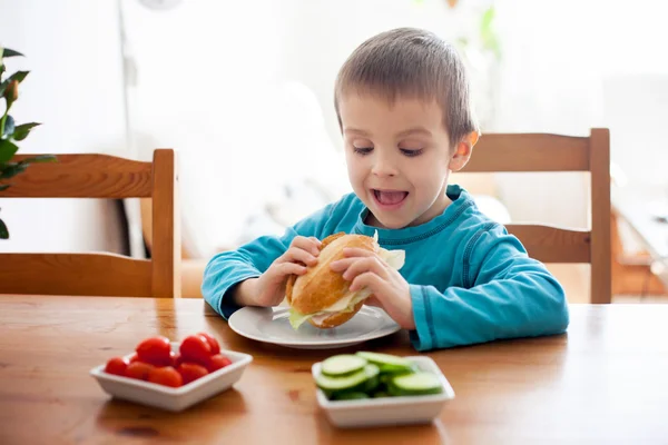 Vacker liten pojke, äta smörgås hemma, grönsaker på den — Stockfoto