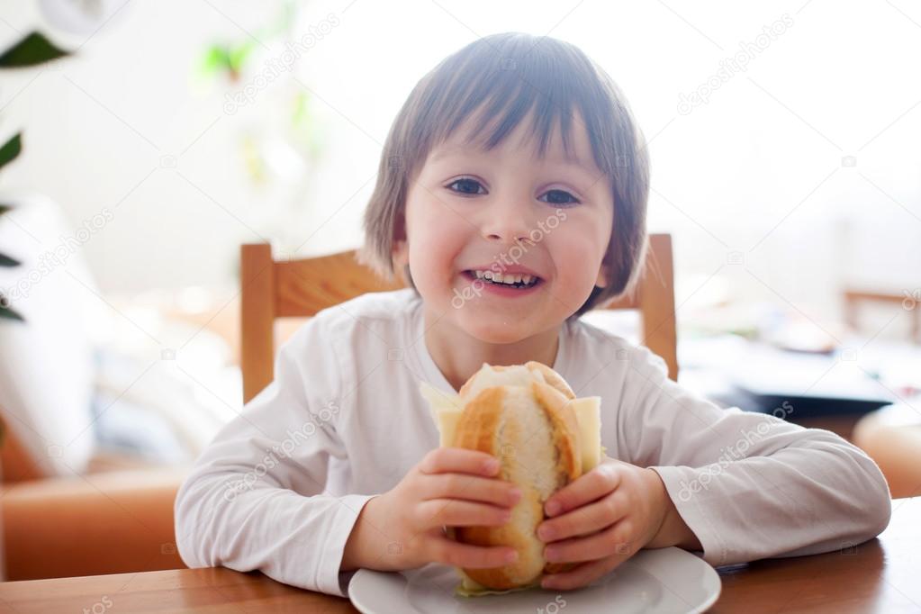 Beautiful little boy, eating sandwich at home, vegetables on the