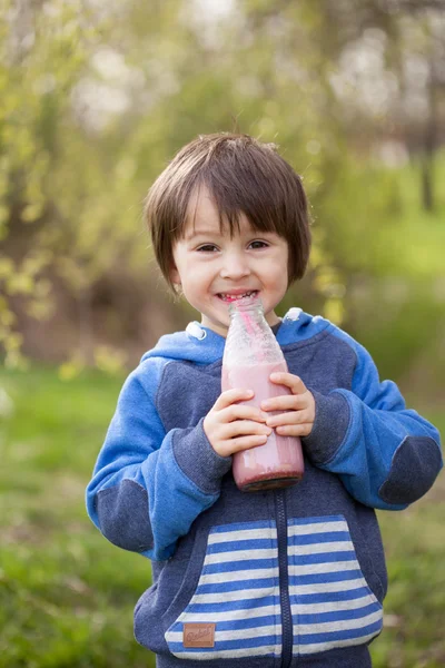 Rapaz bonito, bebendo smoothie de morango saudável no parque — Fotografia de Stock