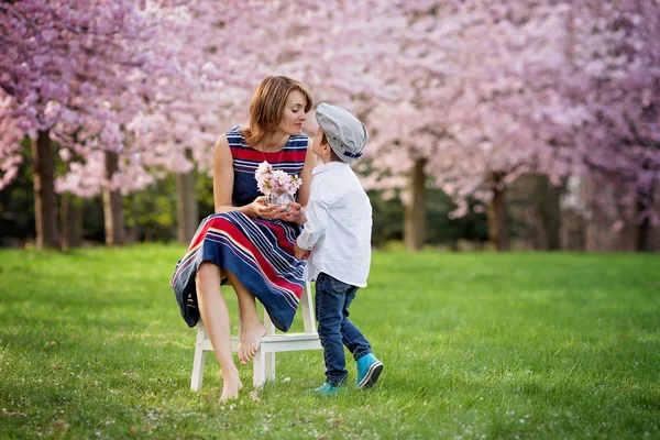 Hermoso niño y mamá en el parque de primavera, flor y presente. Madre. —  Fotos de Stock