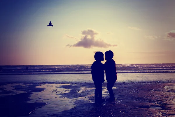Silhuett av två barn, kyssar på stranden — Stockfoto