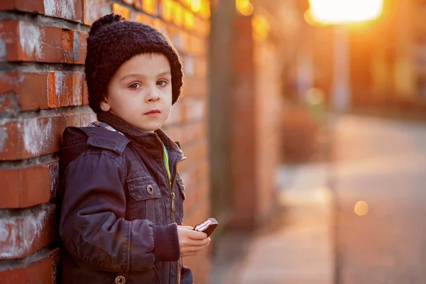 Adorable niño, al lado de la pared de ladrillo, comiendo barra de chocolate en —  Fotos de Stock