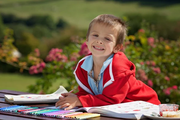 Entzückender Junge in rotem Pullover, der ein Bild in einem Buch zeichnet, in dem — Stockfoto