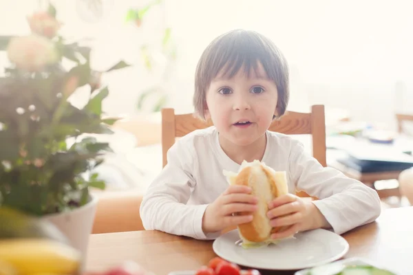 Menino bonito, comendo sanduíche em casa, legumes no — Fotografia de Stock