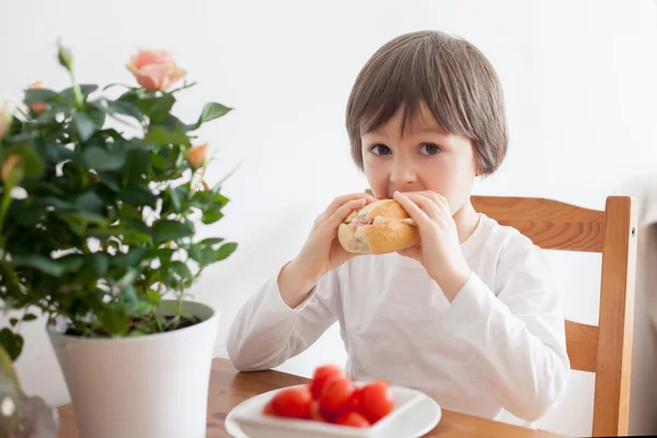 Vacker liten pojke, äta smörgås hemma, grönsaker på den — Stockfoto