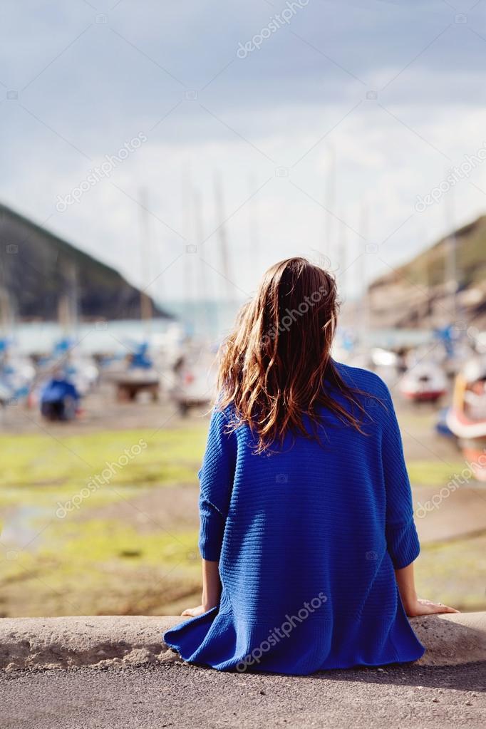 Young woman, sitting on a harbor, looking at the ocean