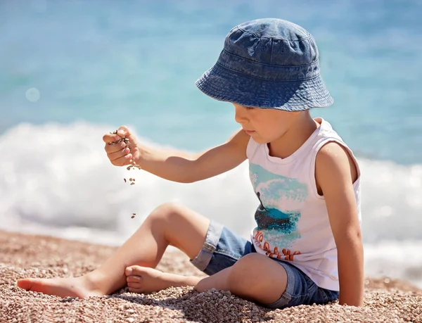 Ragazzo carino, giocando con i ciottoli sulla spiaggia — Foto Stock