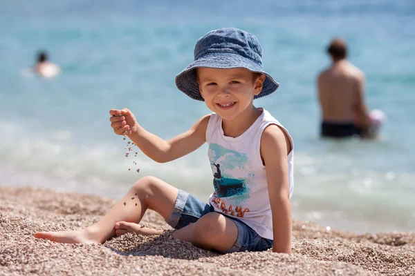 Lindo chico, jugando con guijarros en la playa — Foto de Stock