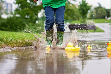 Little boy, jumping in muddy puddles in the park, rubber ducks i clipart