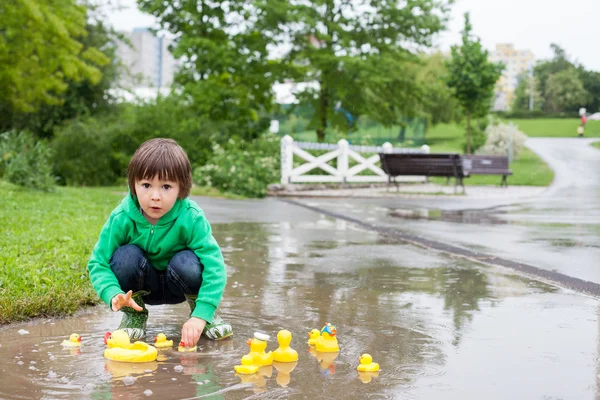Niño, saltando en charcos fangosos en el parque, patos de goma i —  Fotos de Stock