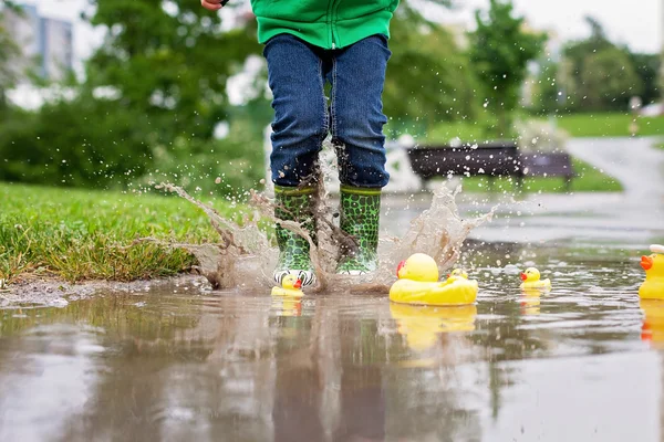 Niño, saltando en charcos fangosos en el parque, patos de goma i — Foto de Stock