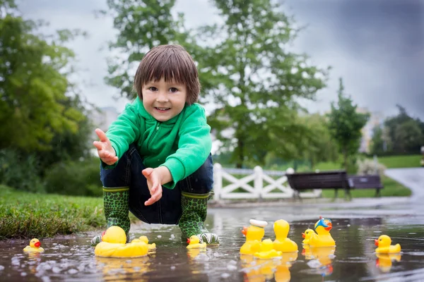 Niño, saltando en charcos fangosos en el parque, patos de goma i — Foto de Stock
