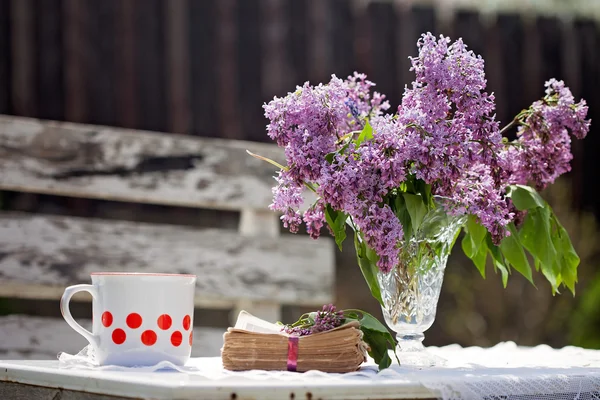 Lilac in a vase on a table, book and coffee mug next to him — Stock Photo, Image