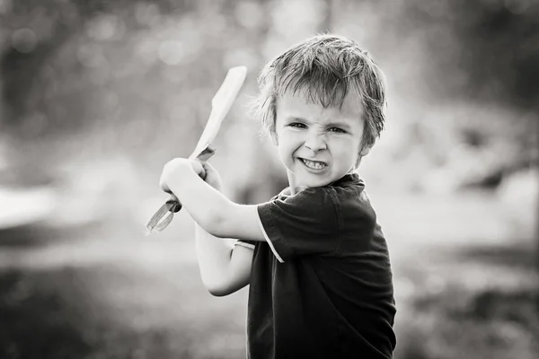 Angry little boy, holding sword, glaring with a mad face at the — Stock Photo, Image