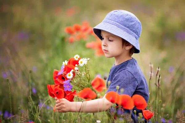 Söt liten pojke med vallmo blommor och andra vilda blommor i vallmo — Stockfoto