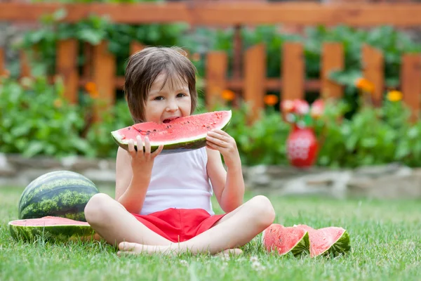 Chlapče jíst meloun v zahradě, přes léto — Stock fotografie