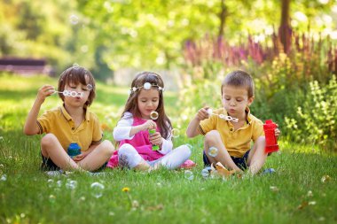 Üç çocuk parkta sabun köpüğü üfleme ve having fun