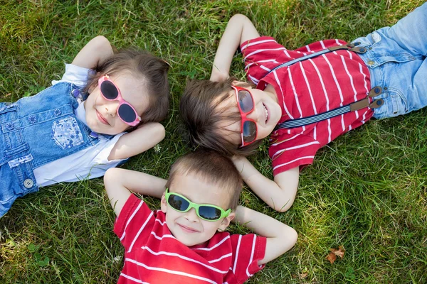 Happy cheerful smiling children, laying on a grass, wearing sung — Stock Photo, Image