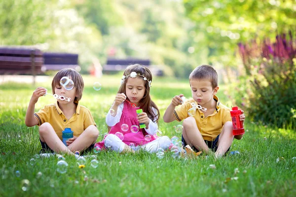 Tres niños en el parque soplando burbujas de jabón y divirtiéndose — Foto de Stock