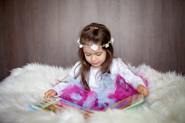 Sweet little girl, sitting in big chair with white fur, reading — Stock Photo, Image