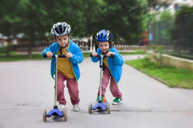 İki sevimli çocuklar, rekabet scooter, parkta açık sürme
