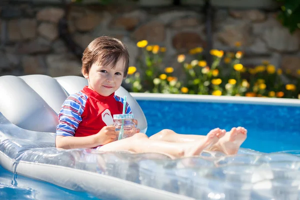 Μικρό αγόρι σε μια μεγάλη πισίνα, πίνοντας χυμό σε ένα καυτό summe — Φωτογραφία Αρχείου