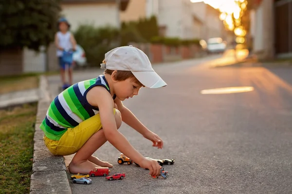 Милый маленький мальчик, играет с маленькими игрушечными машинками на улице на S — стоковое фото