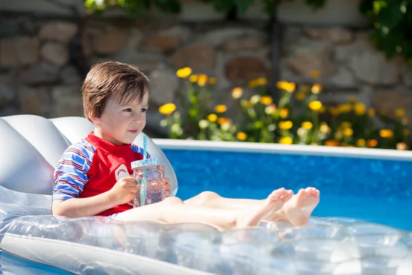 Menino em uma grande piscina, bebendo suco em um summe quente — Fotografia de Stock