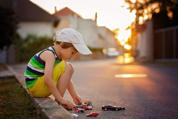 Милый маленький мальчик, играет с маленькими игрушечными машинками на улице на S — стоковое фото