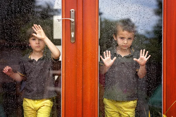 Two little boy, wearing same clothes looking through a big glass — Stock Photo, Image