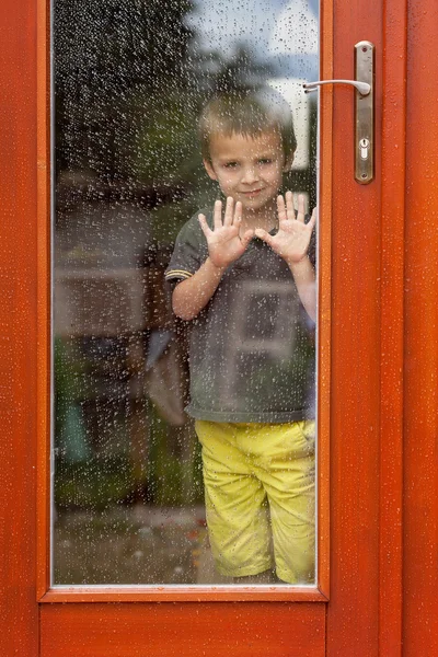 Liten pojke bakom fönstret i regnet — Stockfoto