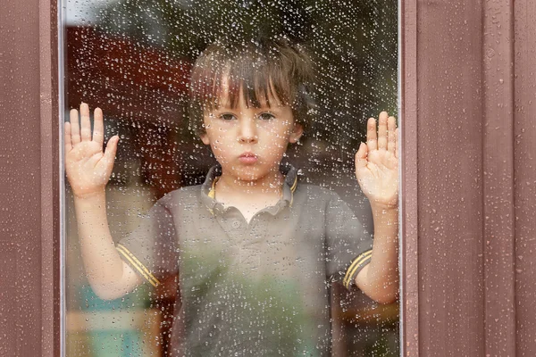 Niño detrás de la ventana bajo la lluvia — Foto de Stock