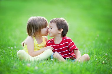 Adorable boy and girl, sitting in the park, smiling and having f