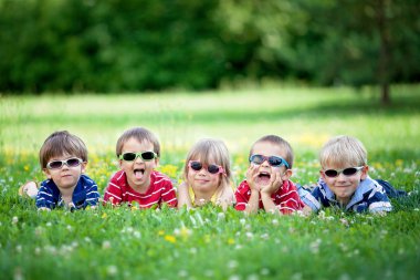 Five adorable kids, lying on the grass, smiling, having fun